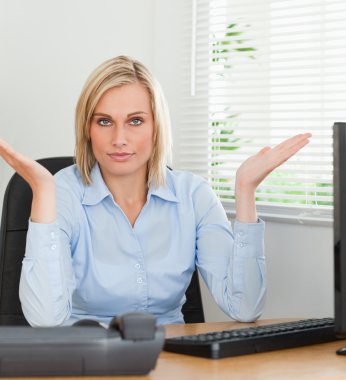 Serious woman sitting behind desk not having a clue what to do n clipart