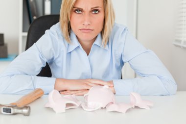 Sad woman sitting in front of an empty shattered piggy bank clipart