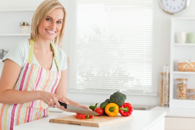 Cute woman cutting red pepper looks into camera clipart