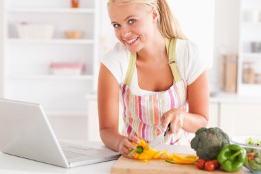 Close up of a blonde woman using a laptop to cook clipart