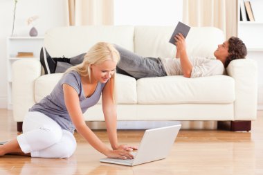 Portrait of a woman using a laptop while her boyfriend is readin clipart