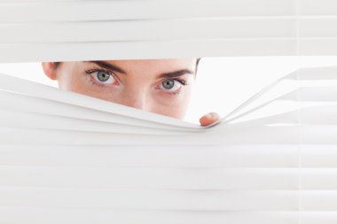 Brunette businesswoman peeking through a venetian blind clipart