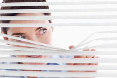 Charming businesswoman peeking through a venetian blind clipart