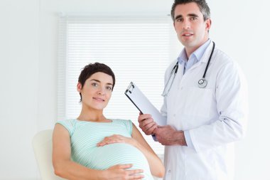 Male Doctor and pregnant patient looking at the camera clipart