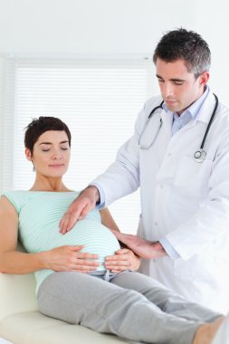 Doctor examining the belly of a pregnant woman clipart