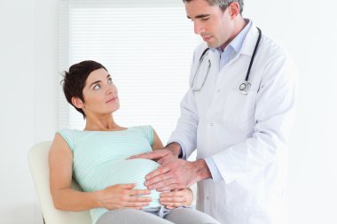 Doctor ausculating a pregnant woman's belly clipart