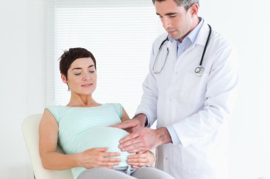 Doctor ausculating a pregnant woman's tummy clipart