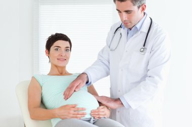 Male Doctor ausculating a pregnant woman's tummy clipart