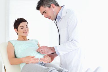 Doctor listening into the woman's tummy with a stethoscope clipart