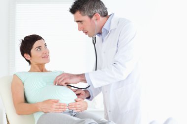 Doctor examining the woman's tummy with a stethoscope clipart