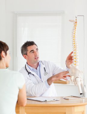 Doctor showing a female patient a part of a spine clipart