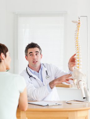 Male Doctor showing a female patient a part of a spine clipart