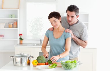 Man massaging his wife while she is cutting vegetables clipart