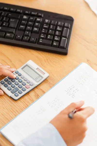 Mãos femininas escrevendo resultados de uma calculadora em um papel — Fotografia de Stock