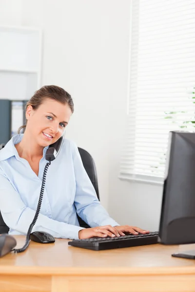 Sekretärin telefoniert, während sie auf ihrer Tastatur tippt — Stockfoto