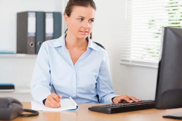 Affärskvinna som sitter bakom sitt skrivbord ser på hennes skärm — Stockfoto