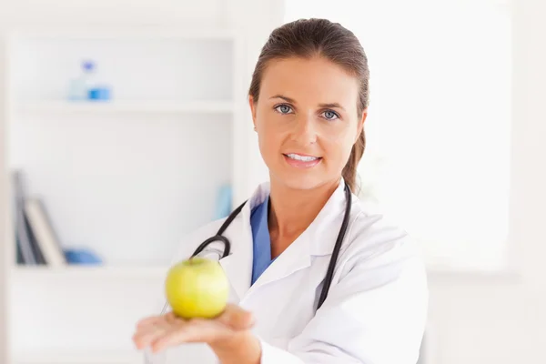 Docteur avec stéthoscope tenant une pomme regardant dans la caméra — Photo