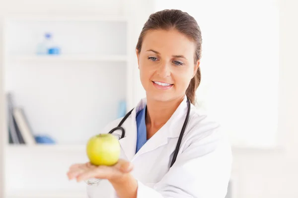 Улыбающийся доктор со стетоскопом, держащий яблоко — стоковое фото