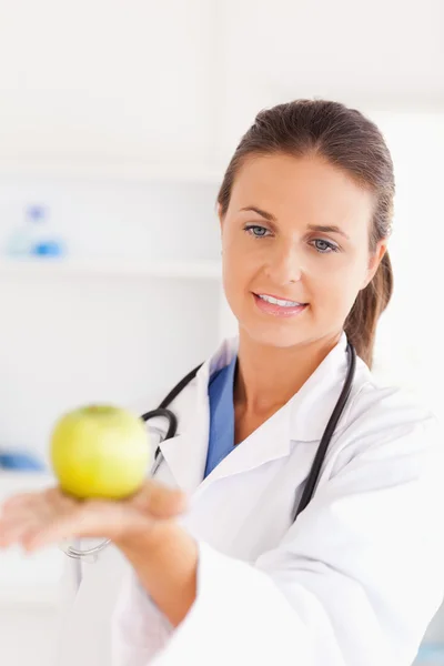 Médico sorridente com estetoscópio olhando para uma maçã — Fotografia de Stock