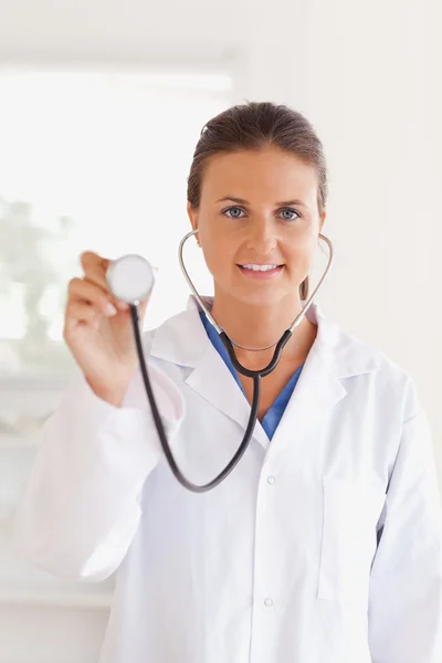 Sorridente medico bruna che presenta uno stetoscopio guardando in th — Foto Stock