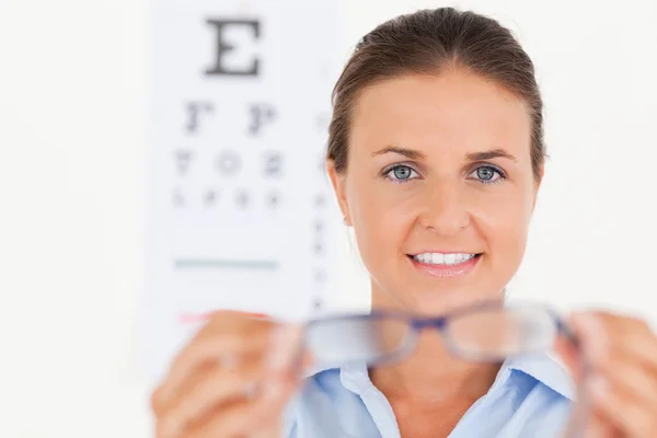 Portrait of a brunette eye specialist handing out glasses lookin — Stock Photo, Image