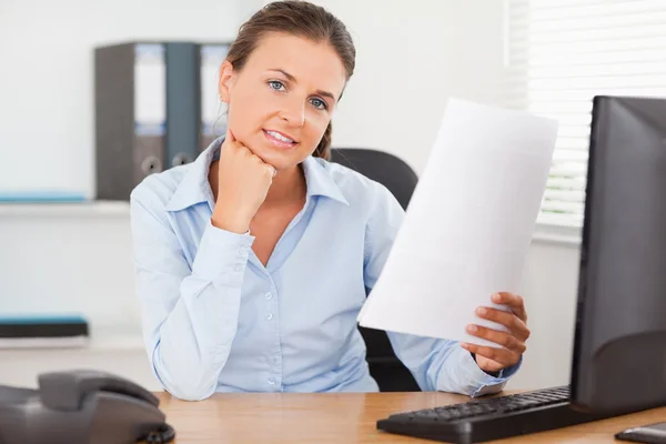 Charming businesswoman holding a paper looking into the camera — Stock Photo, Image