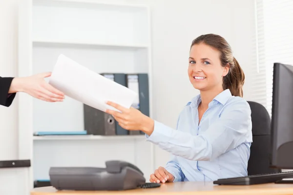 Smiling businesswoman receiving a pile of paper looking into the — Stock Photo, Image