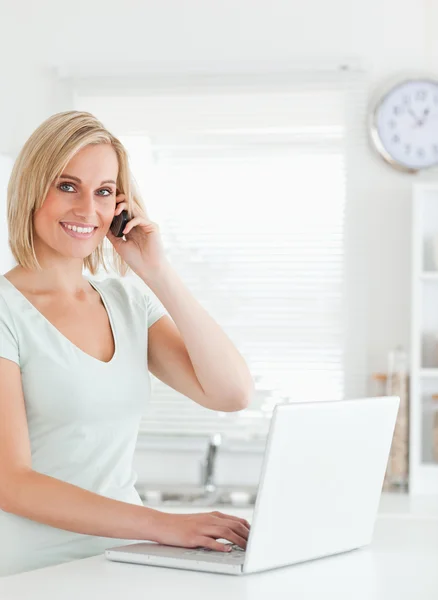 Blond kvinna med en bärbar dator och en telefon som ser in i kameran — Stockfoto