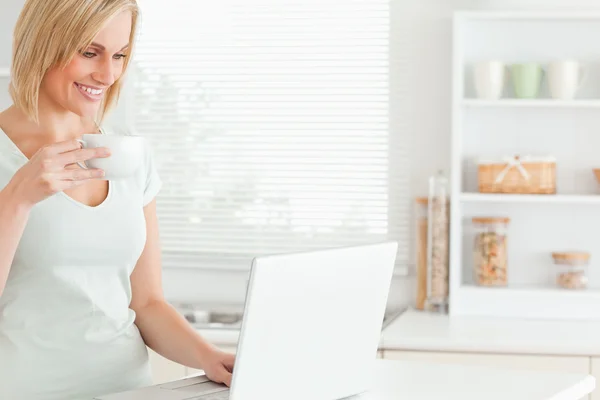 Mulher sorridente com uma xícara de café e um laptop — Fotografia de Stock