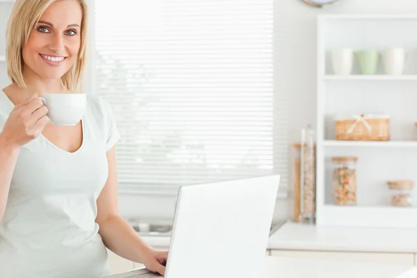 Donna sorridente con una tazza di caffè e un computer portatile guardando nel — Foto Stock
