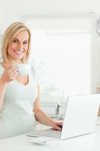 Donna affascinante con una tazza di caffè e un computer portatile guardando in th — Foto Stock