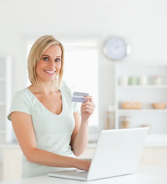 Mulher loira com cartão de crédito e notebook olha para a câmera — Fotografia de Stock