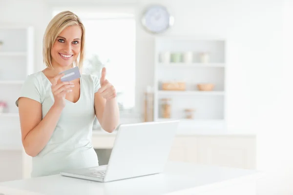 Mulher loira com cartão de crédito e notebook segurando polegar para cima — Fotografia de Stock
