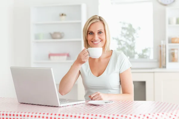 Kvinna dricker kaffe med laptop framför hennes undersöker t — Stockfoto