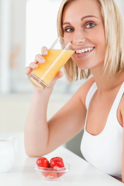 Žena pije sklenici pomerančové šťávy se usmívá na kameru — Stock fotografie