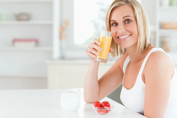 Woman sitting at a table toasting with orange juice looking into — Stock Photo, Image
