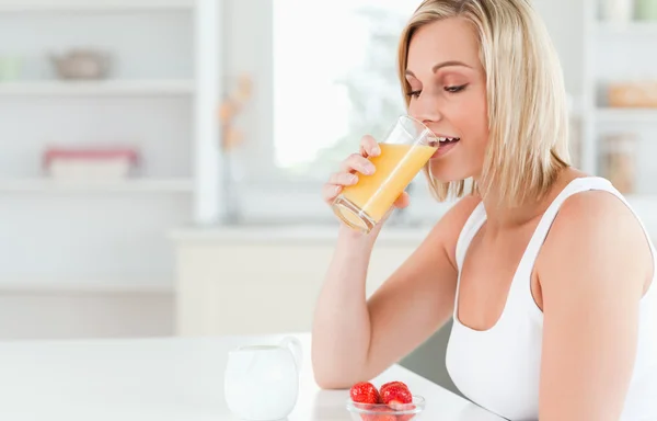 Kobieta siedzi przy stole picia soku pomarańczowego — Zdjęcie stockowe