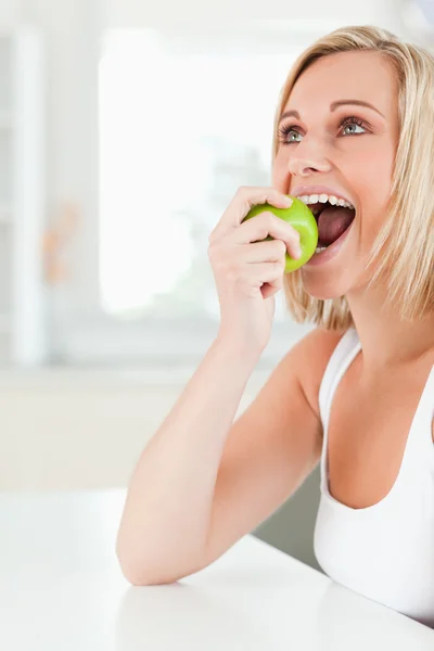 Giovane donna bionda seduta a tavola che mangia una mela — Foto Stock