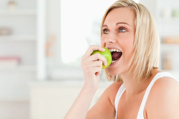Young blonde woman sitting at table eating a green apple — Stock Photo, Image