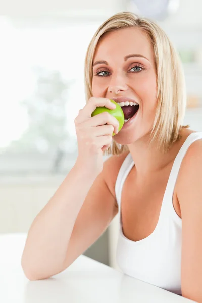 Jovem mulher sentada à mesa comendo uma maçã verde enquanto olha — Fotografia de Stock
