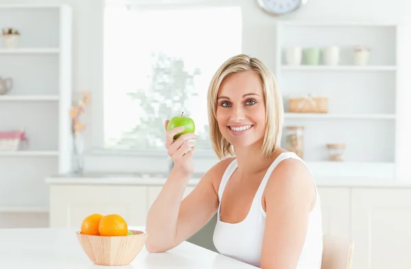 Unga blonda kvinnan håller ett grönt äpple ler in i kameran — Stockfoto