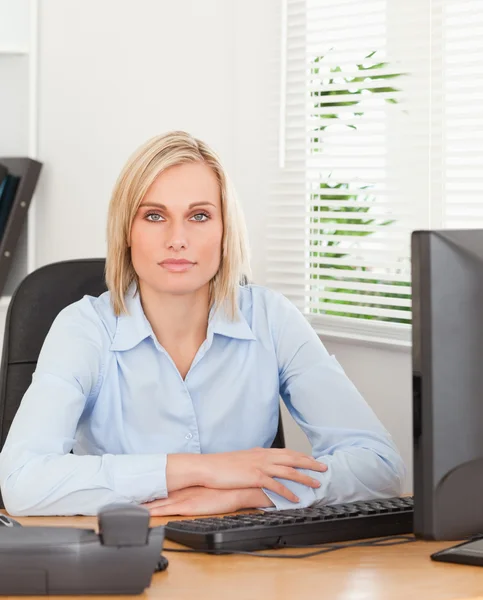 Poważne blond kobieta siedzi za biurkiem — Zdjęcie stockowe