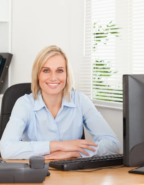 Mujer rubia sonriente sentada detrás de un escritorio —  Fotos de Stock