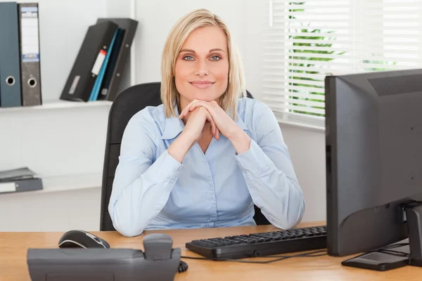 Mujer sonriente con barbilla en las manos detrás de un escritorio —  Fotos de Stock