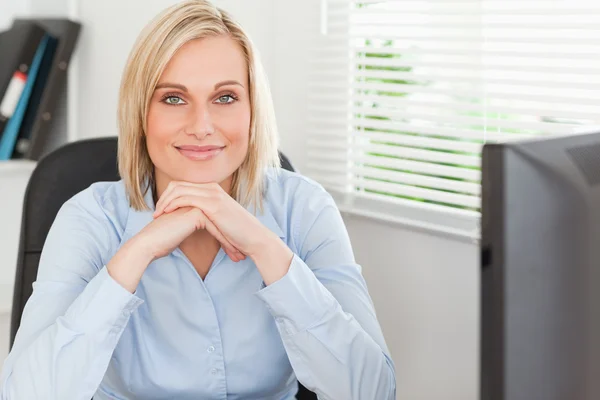 Niedliche blonde Frau mit Kinn an den Händen hinter einem Schreibtisch — Stockfoto