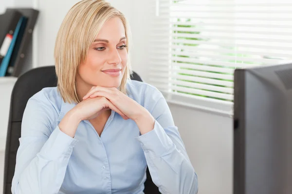 Femme blonde mignonne avec le menton sur les mains derrière un bureau à la recherche d'un — Photo