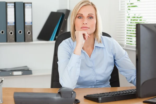 Serious woman with chin on hand behind a desk — Stock Photo, Image