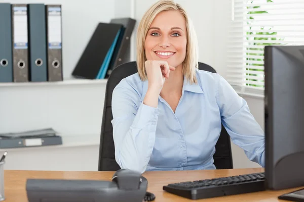 Femme souriante avec le menton à la main derrière un bureau — Photo