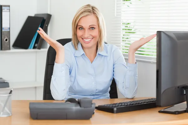 Χαμογελώντας ξανθιά γυναίκα που κάθεται πίσω από το γραφείο δεν έχουν ιδέα τι — Φωτογραφία Αρχείου