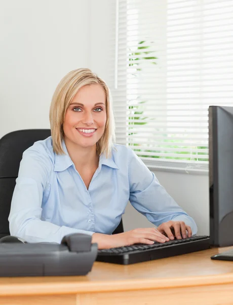 Arbeitende blonde Frau blickt vor einem Bildschirm in die Kamera — Stockfoto
